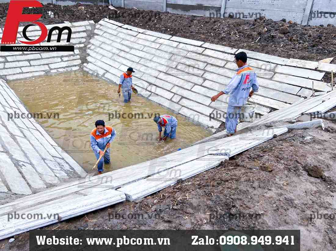 Công nhân thi công lắp ghép tấm tường bê tông làm bờ kè ao nuôi thủy sản.