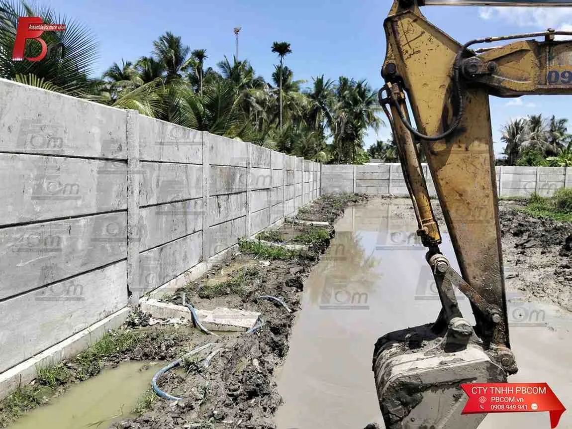 Xe xúc cơ giới hỗ trợ ép móng neo và thi công tường bao bê tông lắp ghép dọc theo rãnh sình lầy.